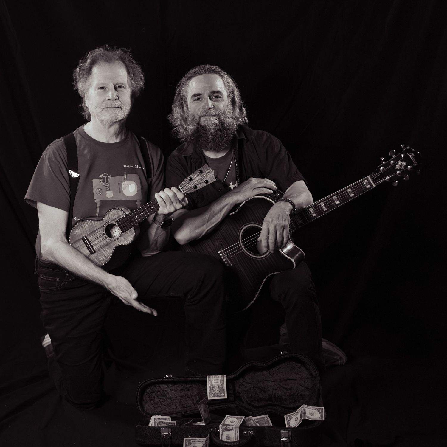 Two musicians pose with acoustic guitar and ukulele in black and white studio portrait.