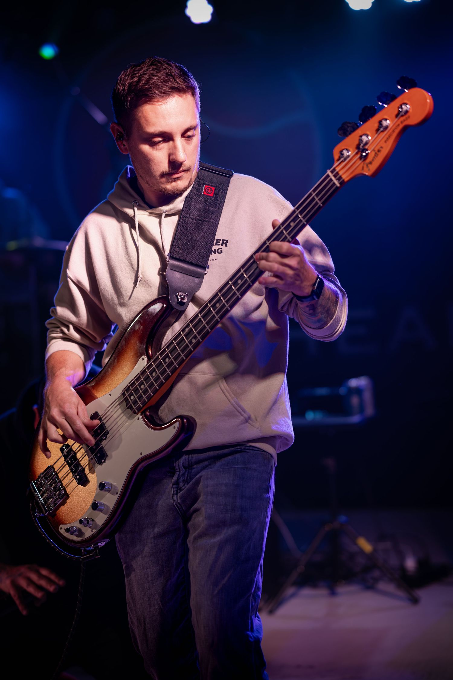 Bass player performing on stage in white hoodie under blue concert lighting. Marblehead Band
