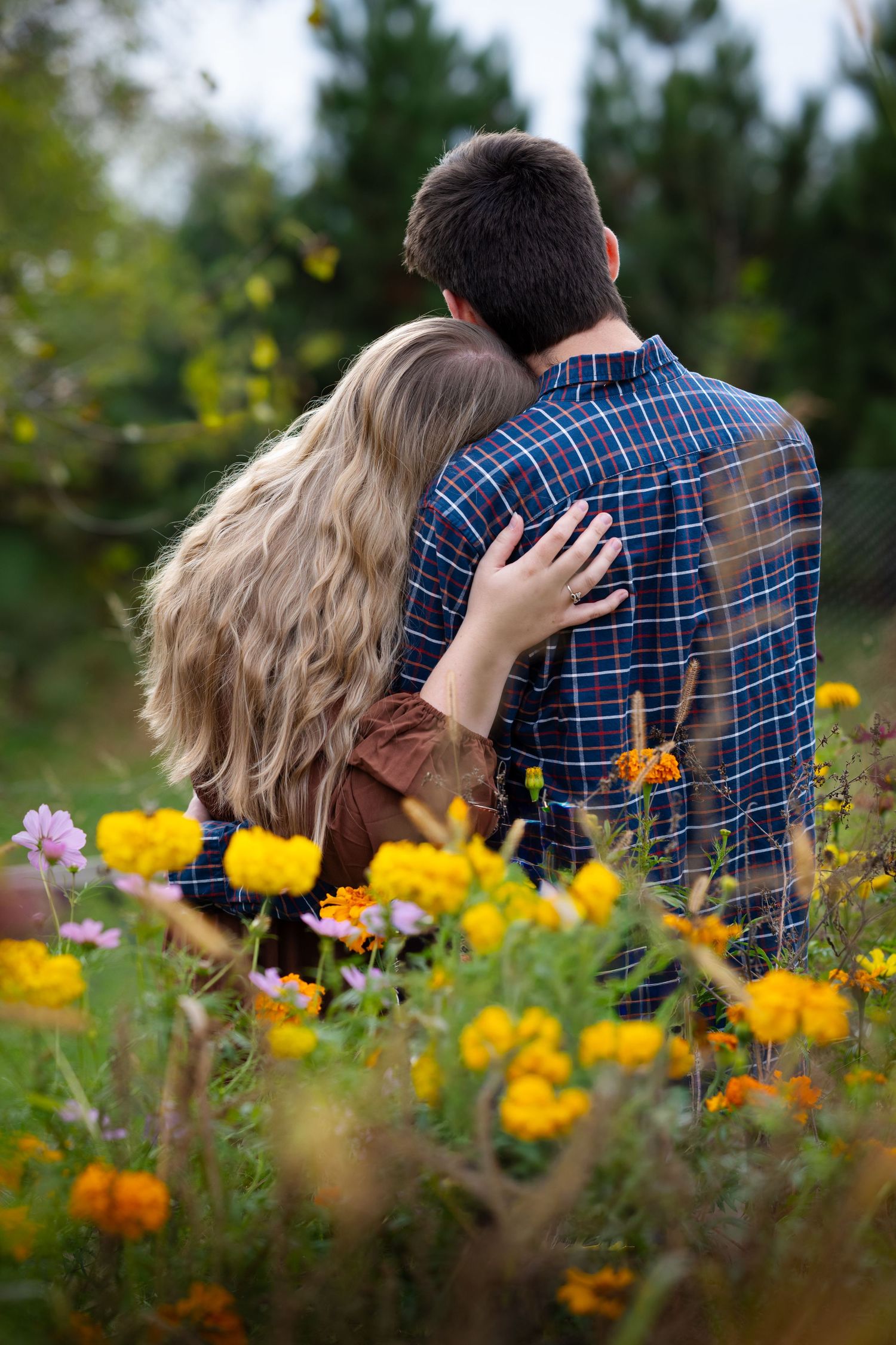 A couple embraces romantically in a vibrant flower field surrounded by yellow and pink blooms.