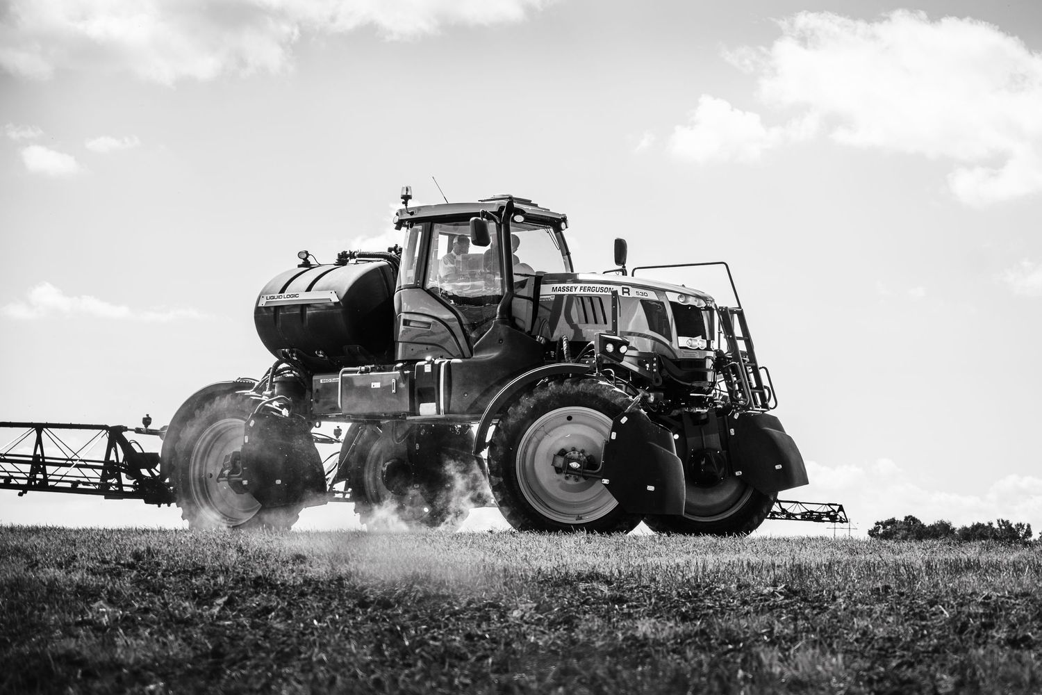 Series of tractors working in a dusty agricultural field under cloudy skies. Massey Ferguson 530R sprayer.