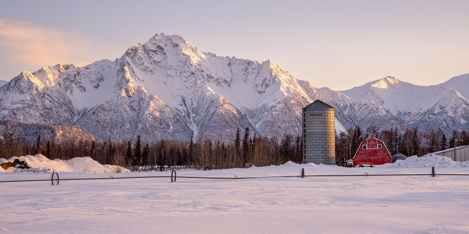 Snowy mountain landscape with red barn and winter scenery at sunset. Pioneer Peak Palmer Alaska