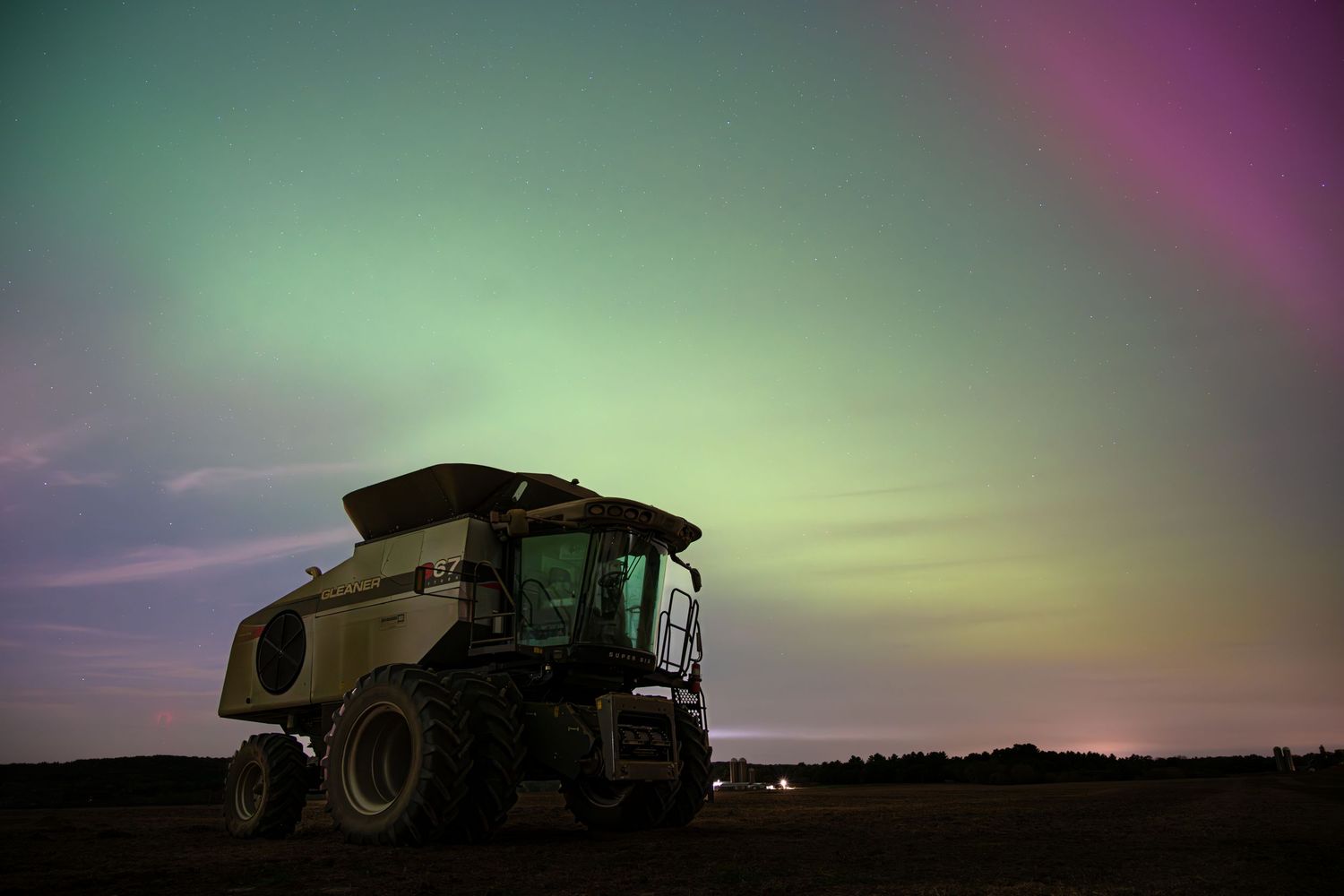 Farm combine silhouetted against colorful aurora borealis in night sky. Gleaner s67 in Wisconsin.