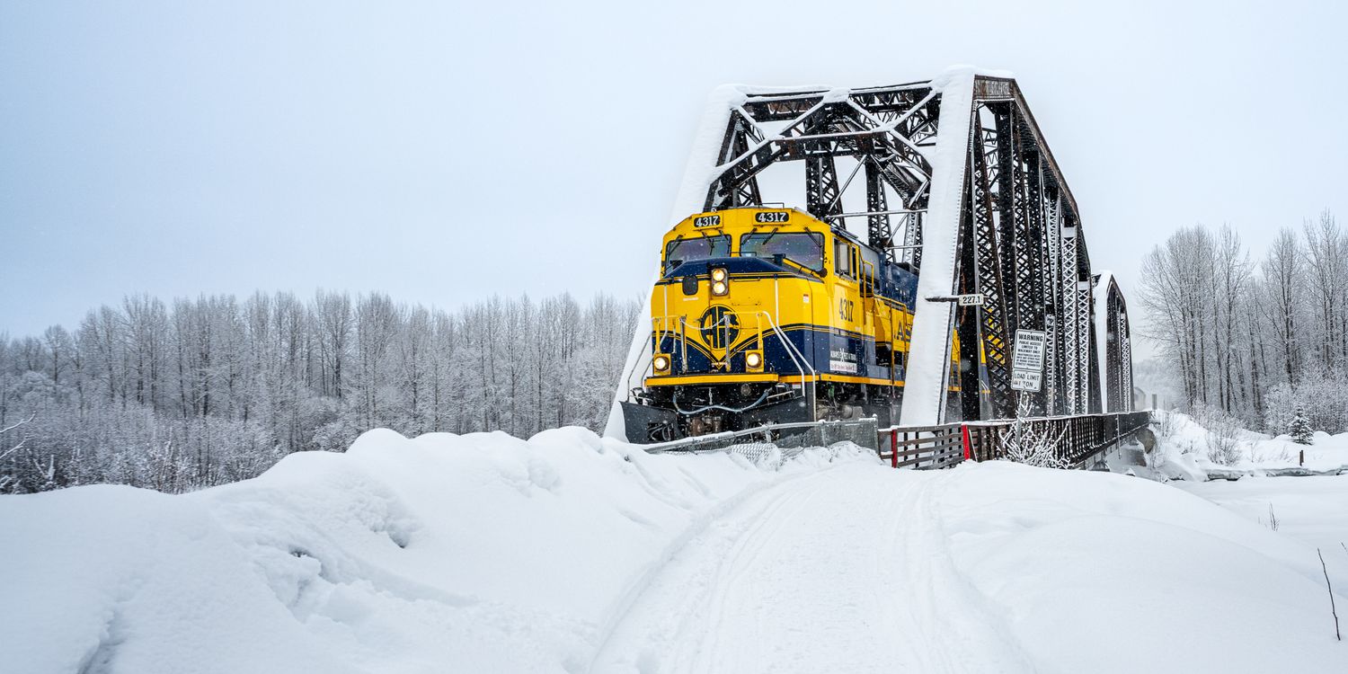 Snow-covered train tracks with yellow locomotive pushing through deep winter drifts. Alaska Railroad in Talkeetna Alaska.
