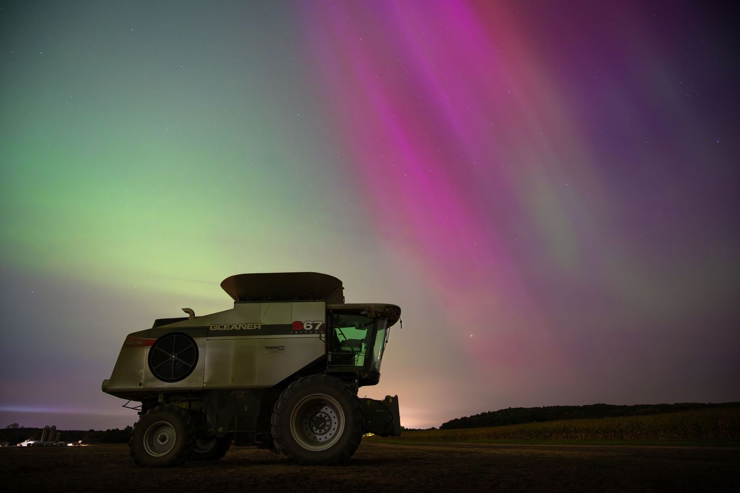 Silhouette of farm equipment against colorful aurora borealis in the night sky.