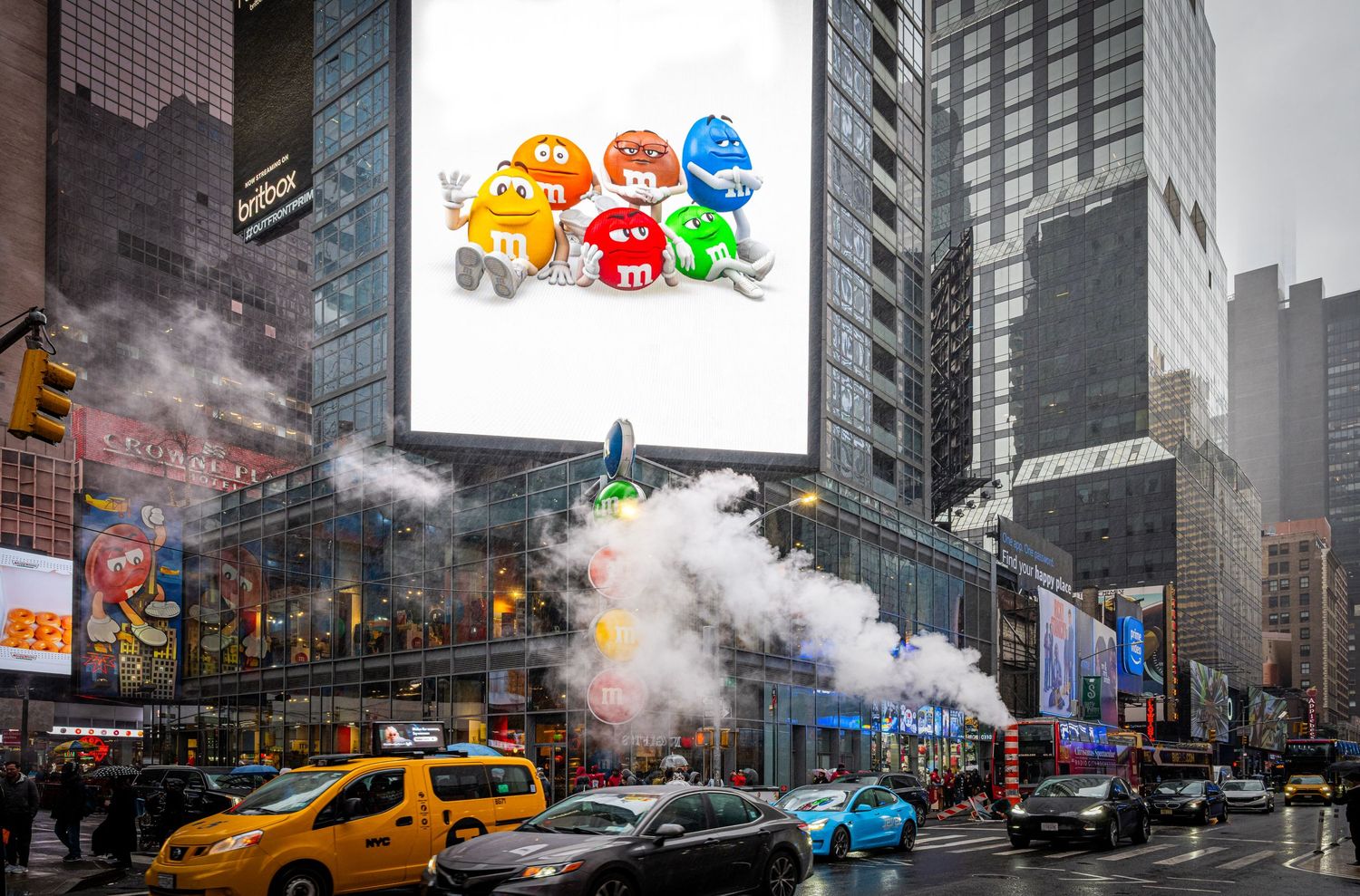 Busy New York City street scene with yellow taxis and steam rising from manholes on a cloudy day.