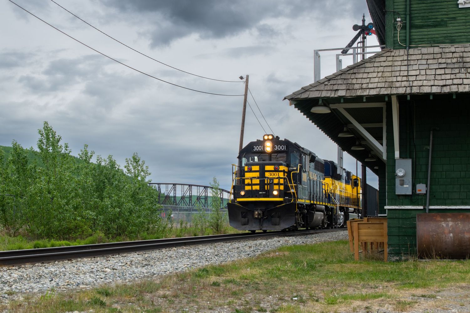 Freight trains passing through rural railway station under cloudy skies. Alaska Railroad GP40-2 Nenana depot.