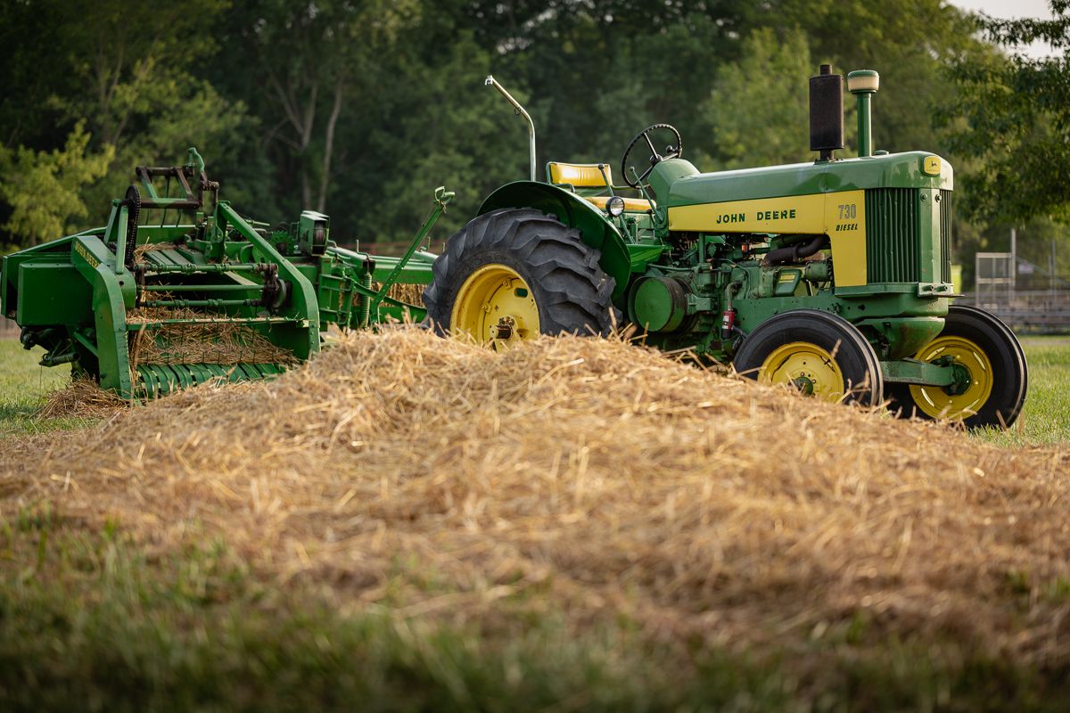 Classic green John Deere tractor with hay equipment in golden field.