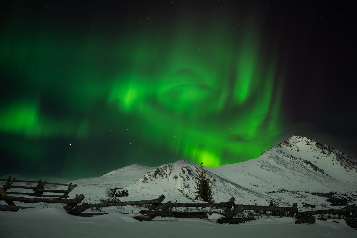 Spectacular green aurora borealis dancing over snowy mountain peaks.