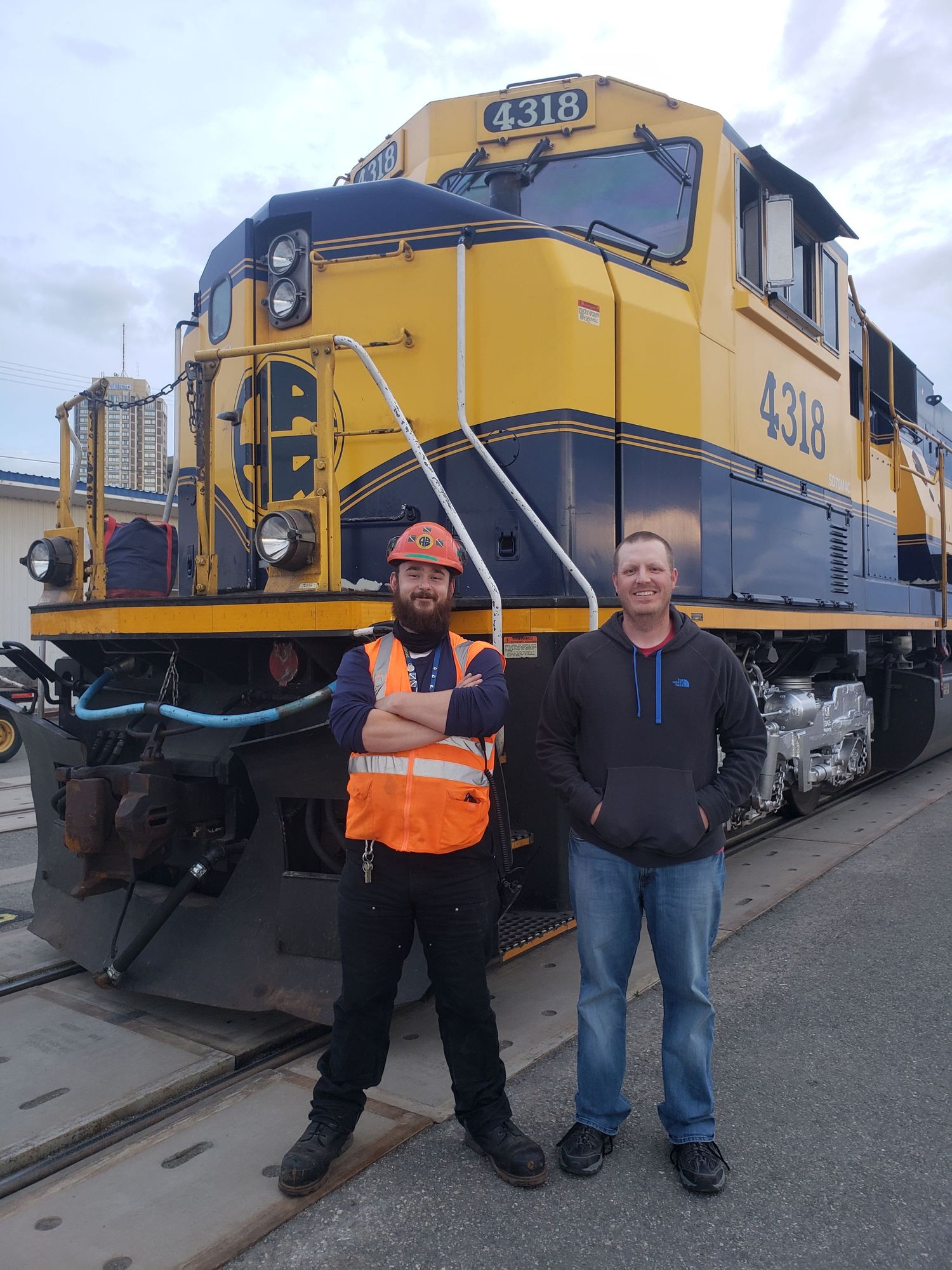 Yellow diesel locomotives lined up at a railway yard with workers in safety gear. Alaska Railroad SD70MAC Anchorage depot.