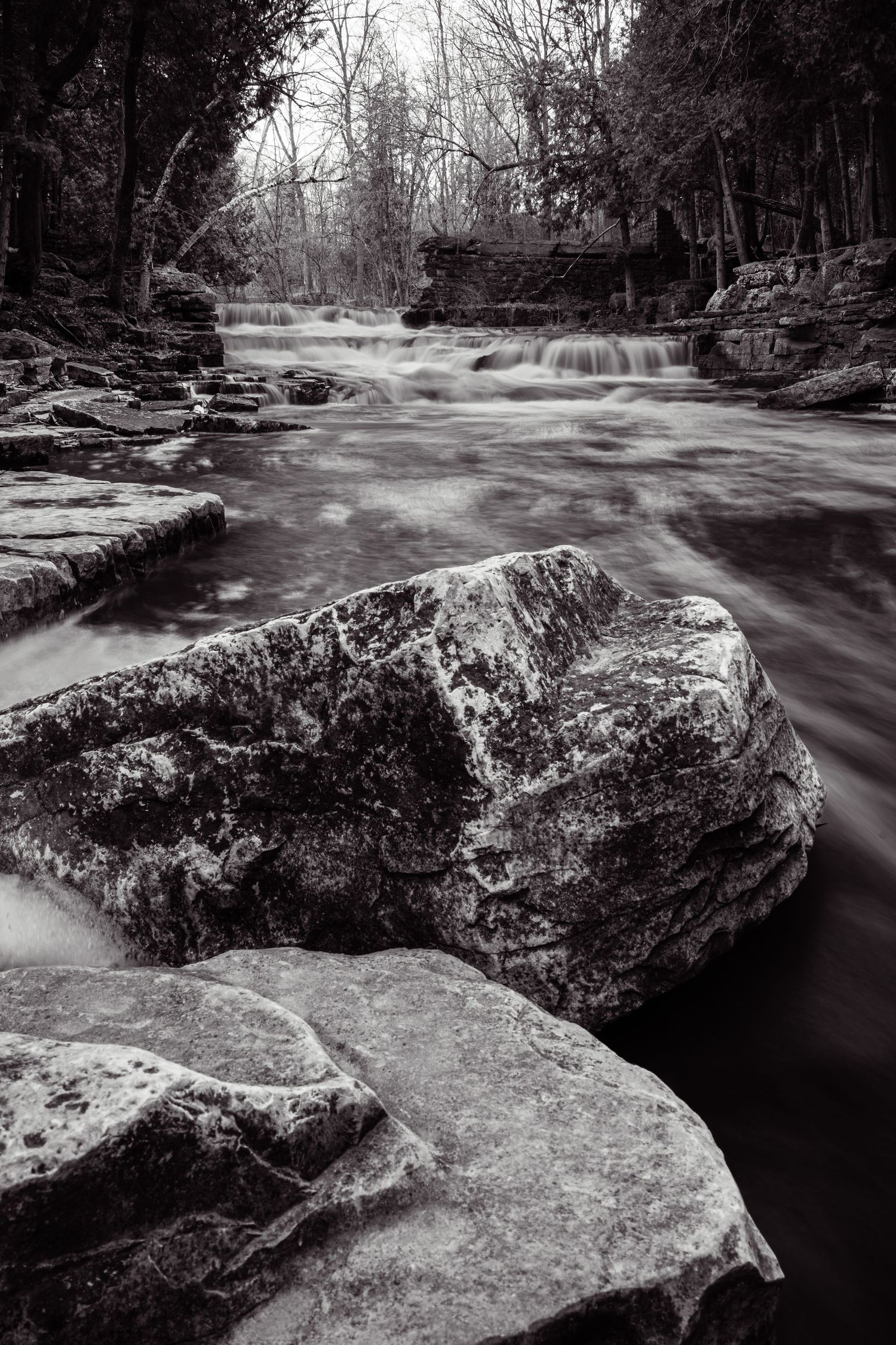 Black and white landscape of rushing water flowing over rocky terrain in a forest stream.