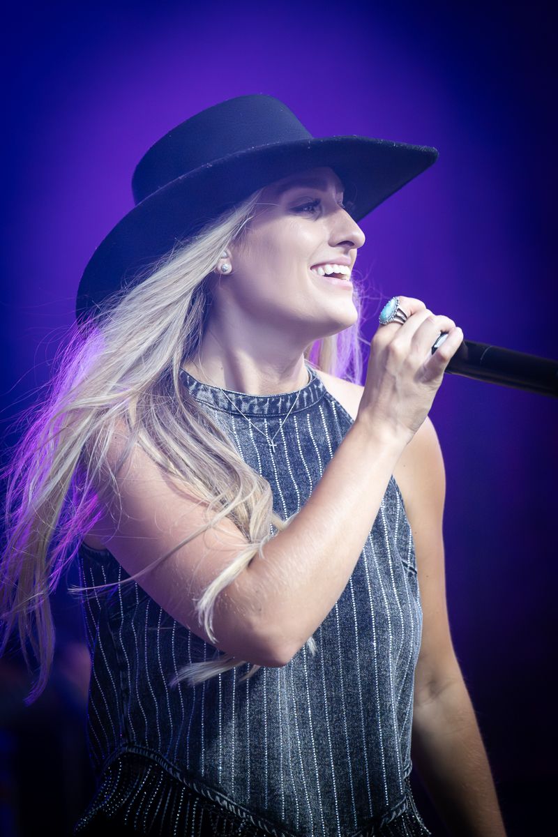 A performer in a pinstriped outfit and baseball cap sings on stage with purple lighting effects. Grand Union.