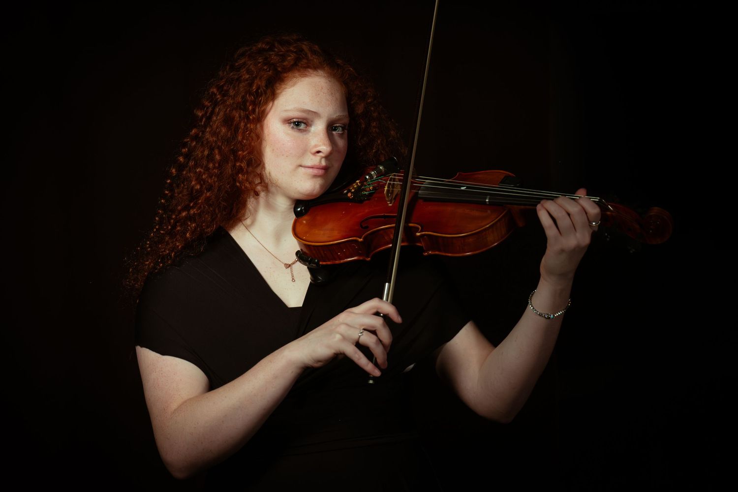 A violin performance captured in moody lighting against a black background.