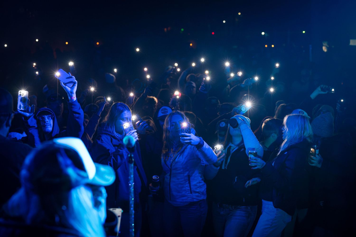 Nighttime crowd scene with glowing phone lights and blue illumination creating a starry effect.