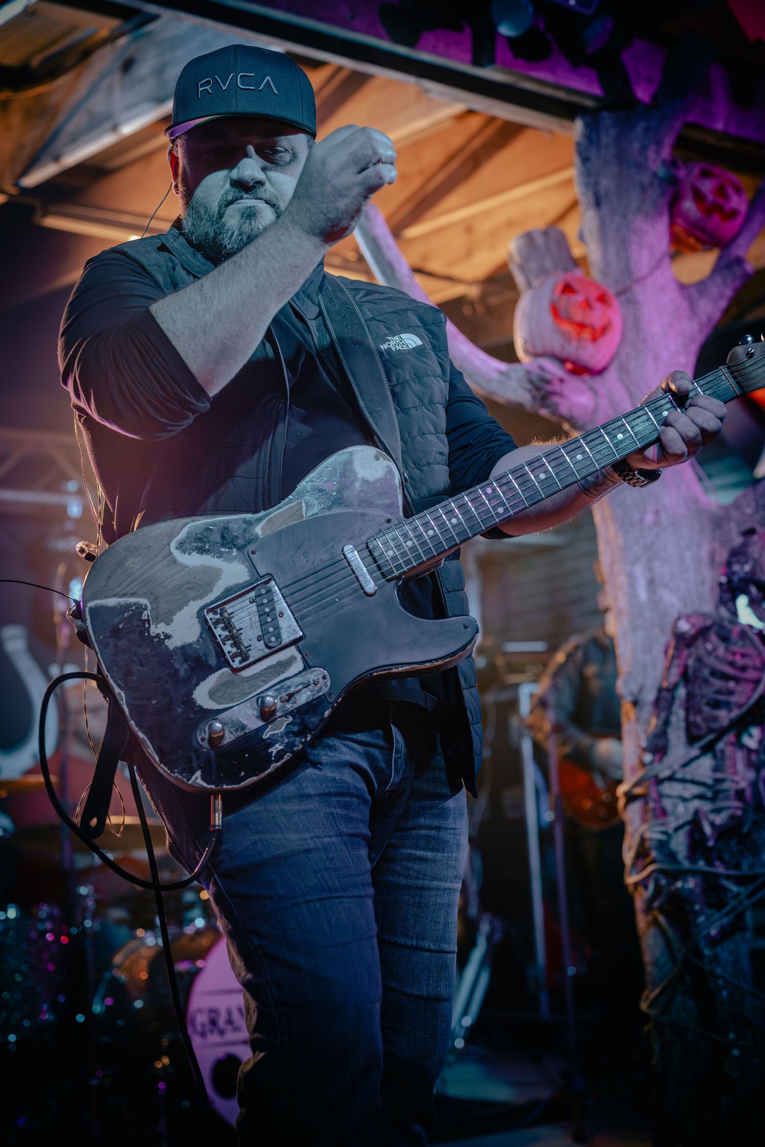 Close-up of guitarist playing electric guitar on stage with purple mood lighting. Grand Union