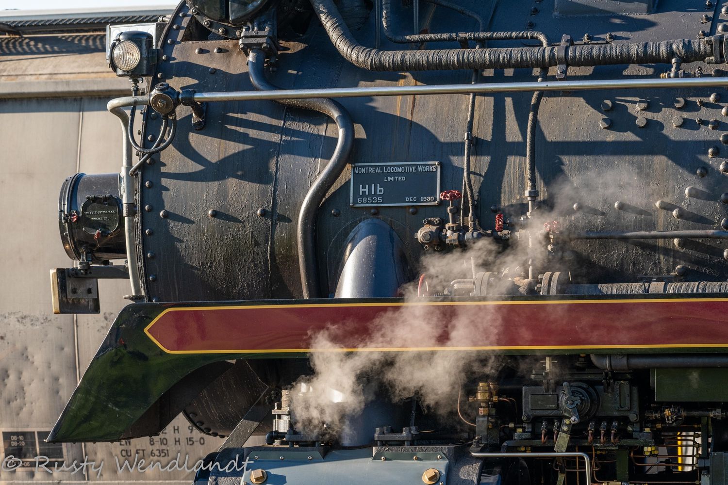 Industrial factory complex with steam rising from multiple smokestacks against dark sky. Canadian Pacific 2816 steam locomotive.