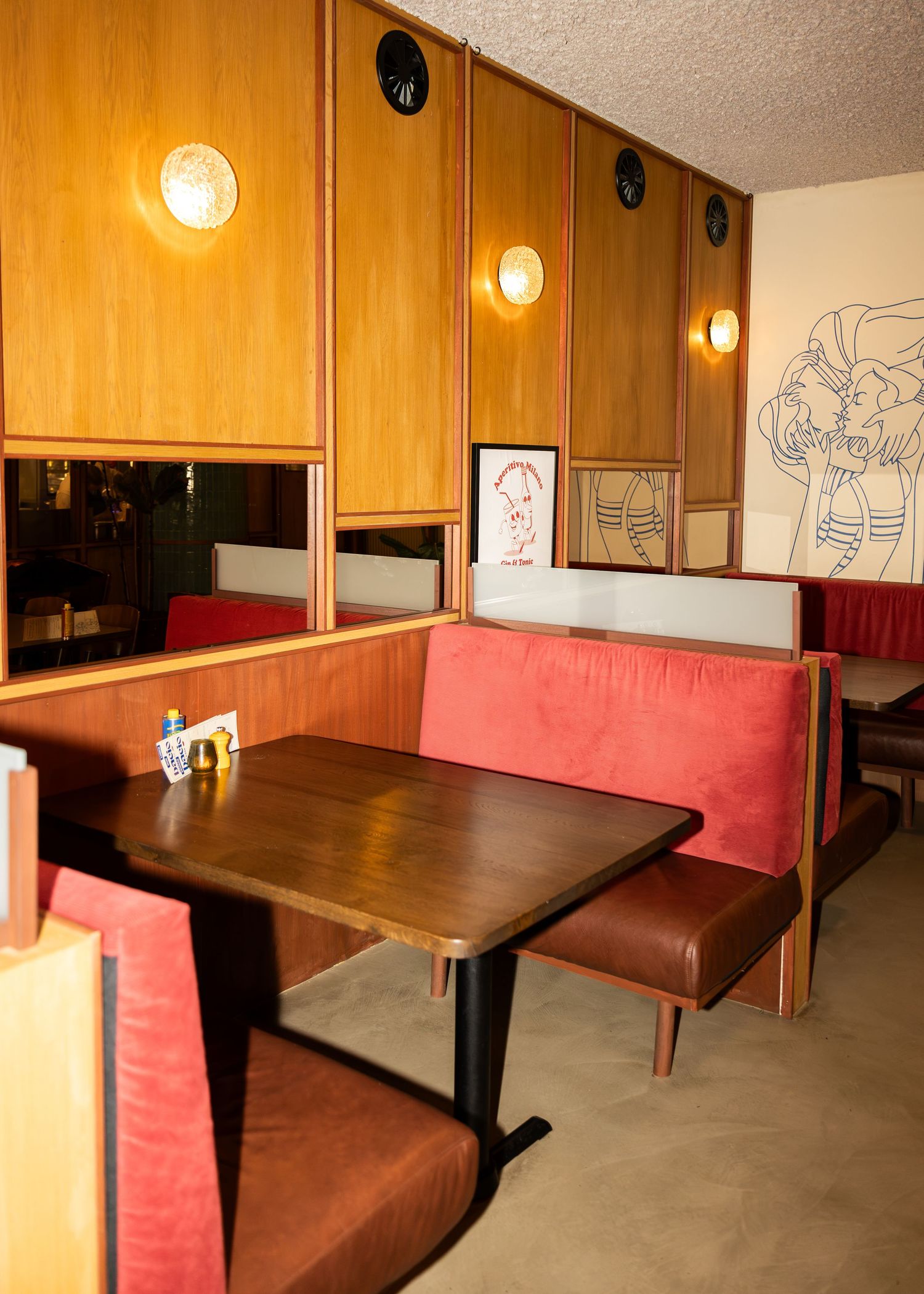 Retro diner booth seating with red upholstery, wooden paneling, wall sconces, and decorative artwork in a cozy restaurant.