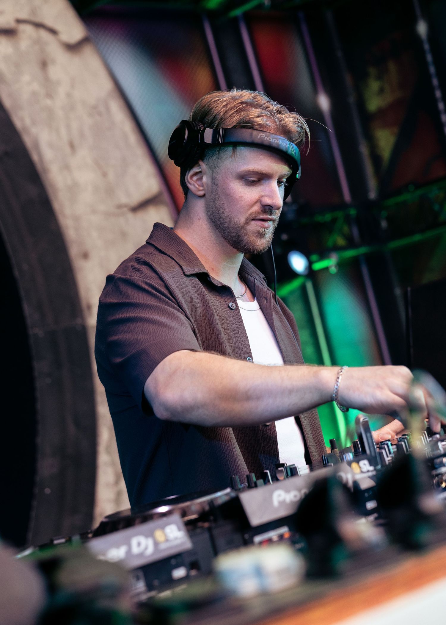 A DJ wearing headphones operates Pioneer DJ equipment at an outdoor music festival event. Festival photography,