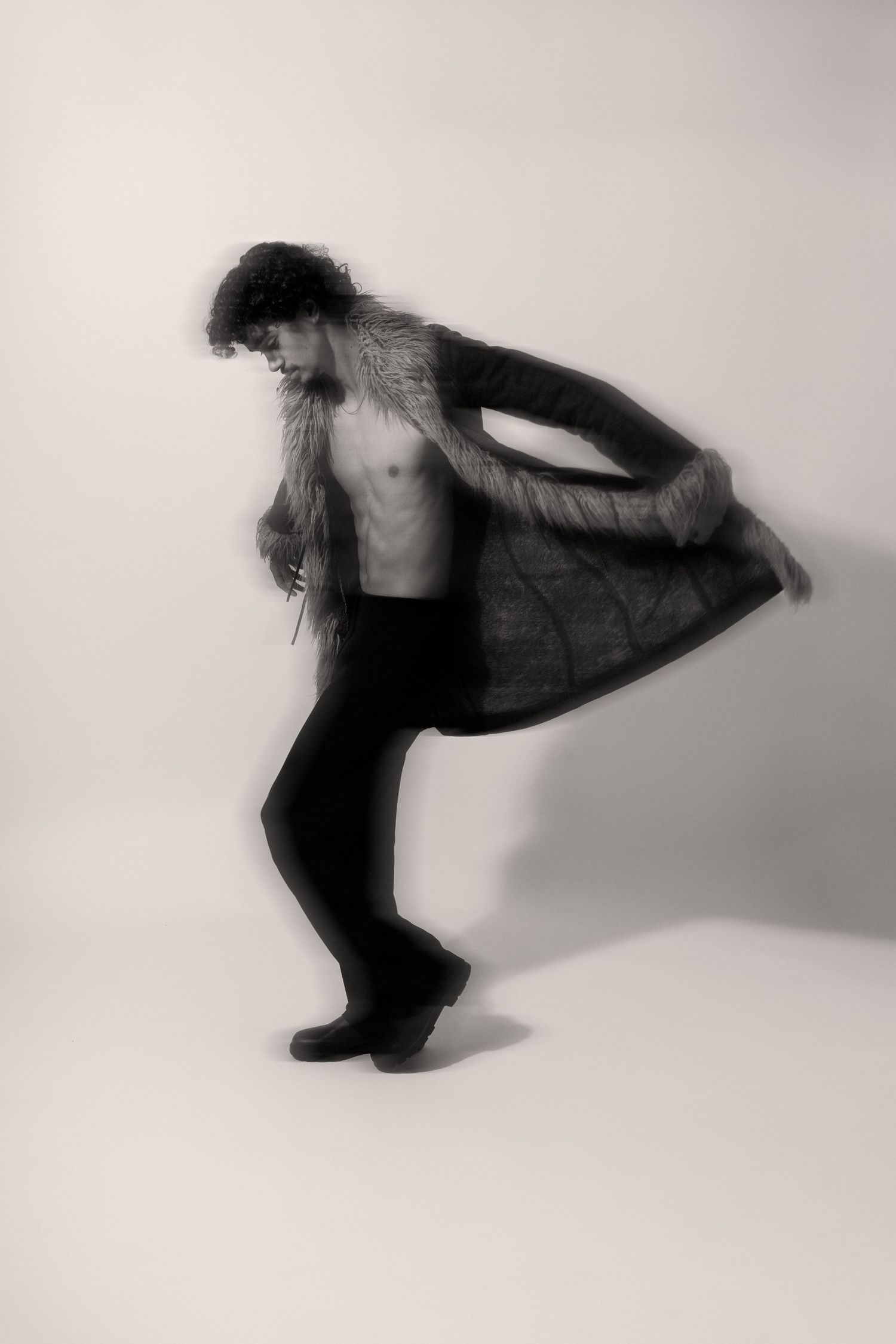 Black and white photo of a shirtless man in a fur coat posing dynamically in a studio setting.  fashion photography, netherlands