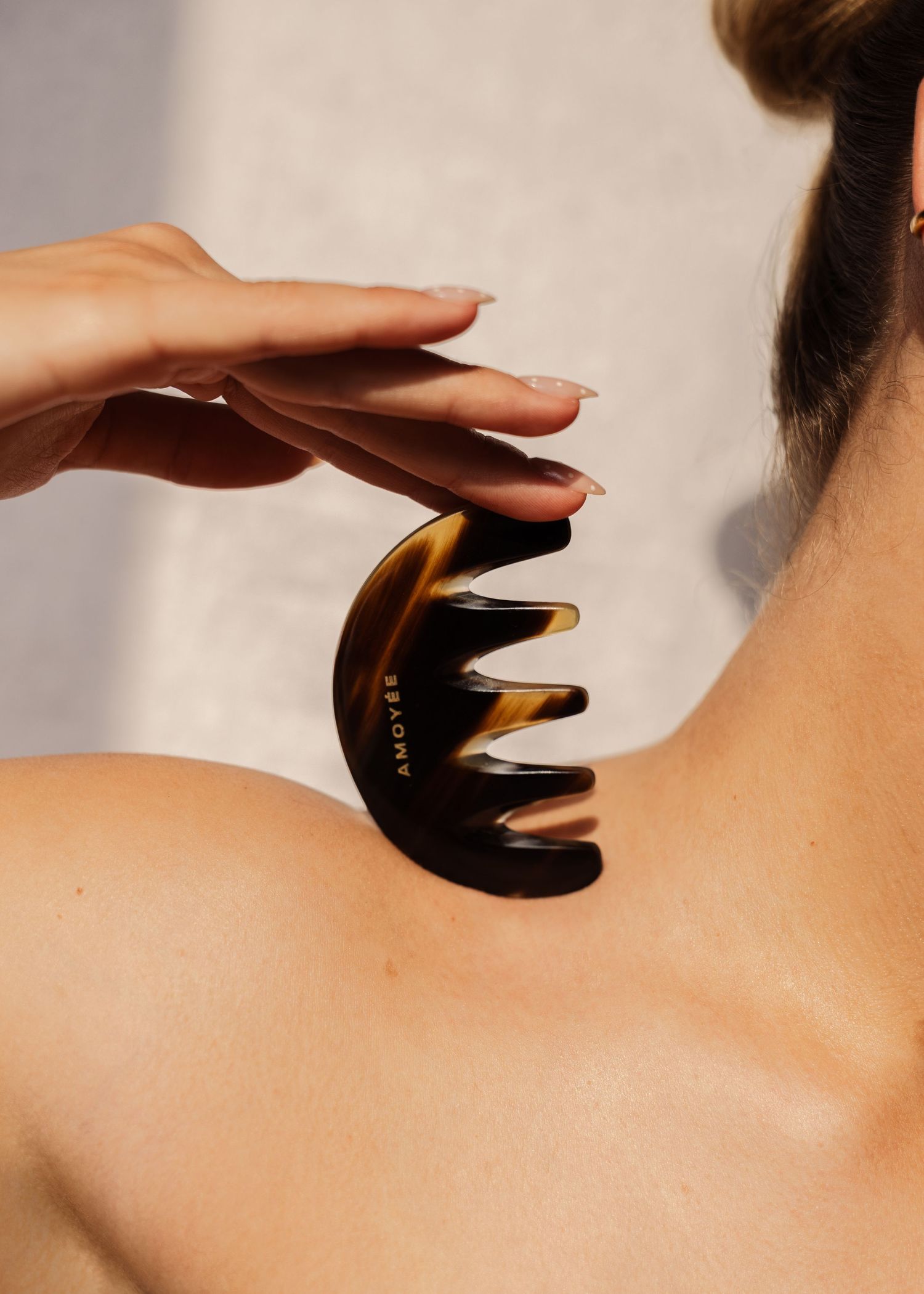 Woman using a tortoiseshell comb gua sha tool on her upper back and neck for muscle relief and relaxation.  fashion photography, netherlands