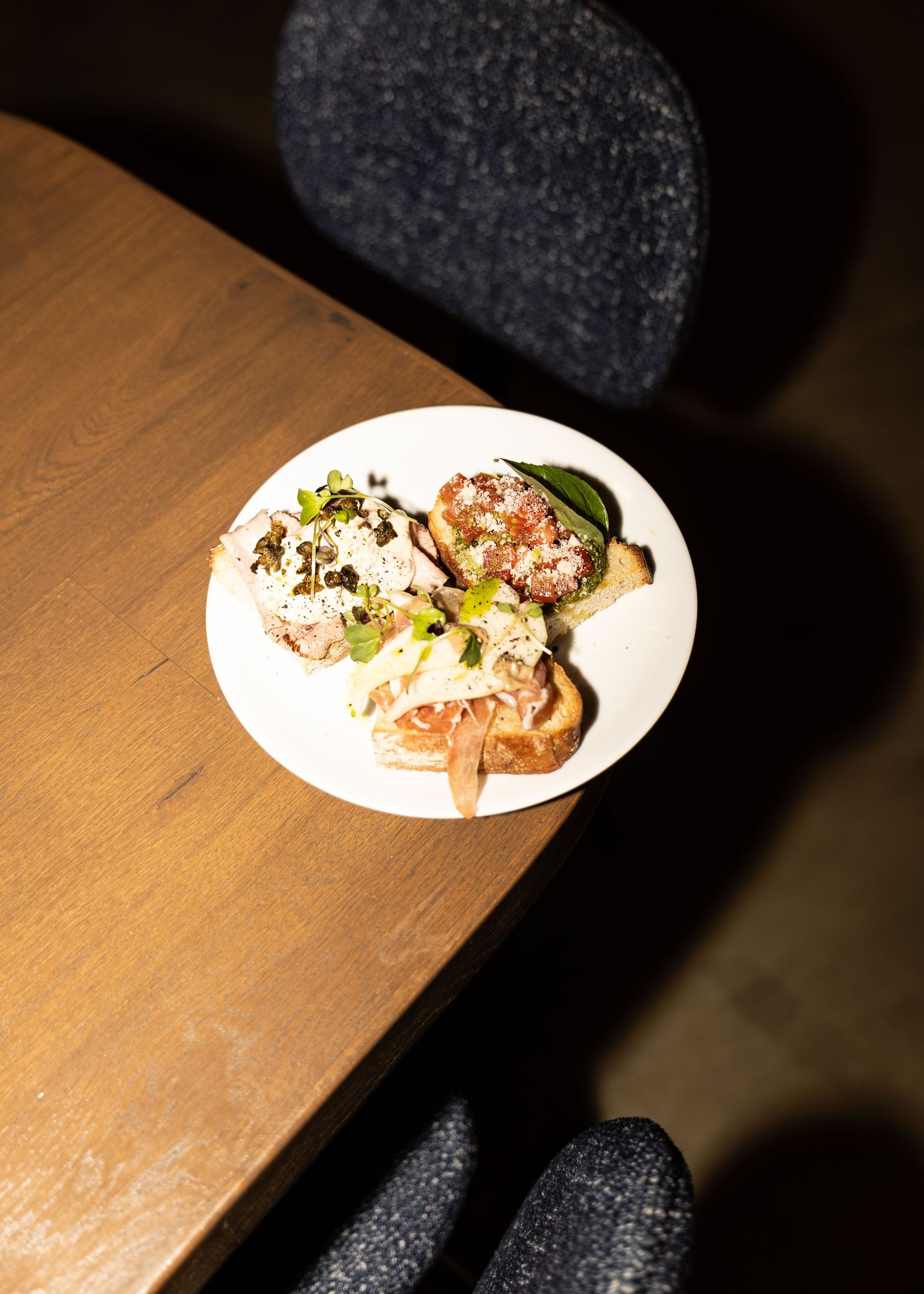 Elegant white plate with gourmet appetizers garnished with fresh herbs on a wooden restaurant table.
