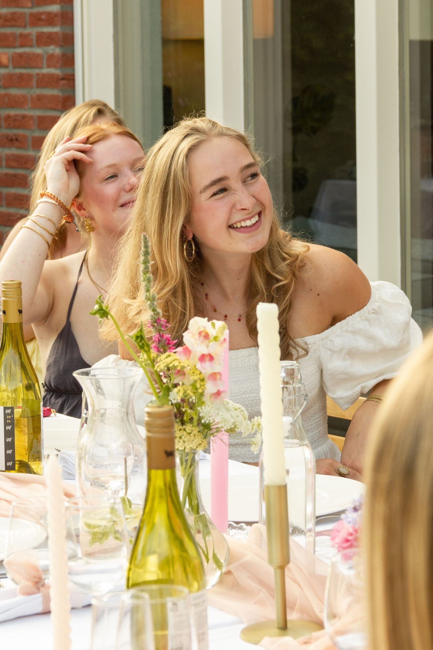 Two young women laughing and enjoying an outdoor garden party with candles and flowers on the table.  event photography, netherlands