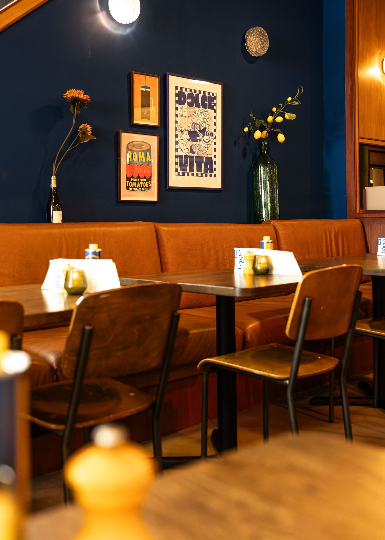 Cozy restaurant interior with brown leather banquette seating, dark wood tables, and navy blue walls adorned with vintage posters.