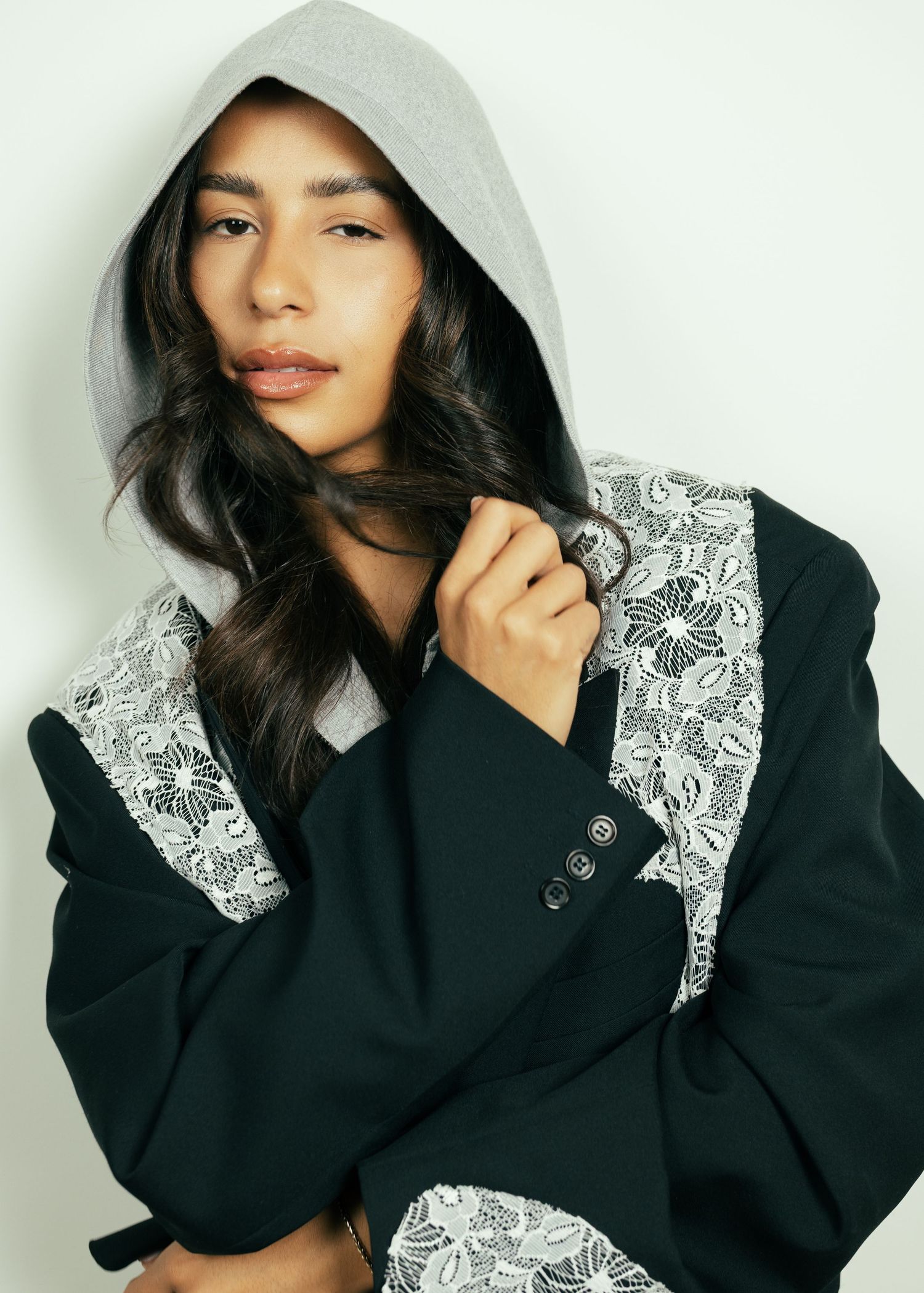 Young woman in black hooded jacket with lace detailing, posing against white background.  fashion photography, netherlands