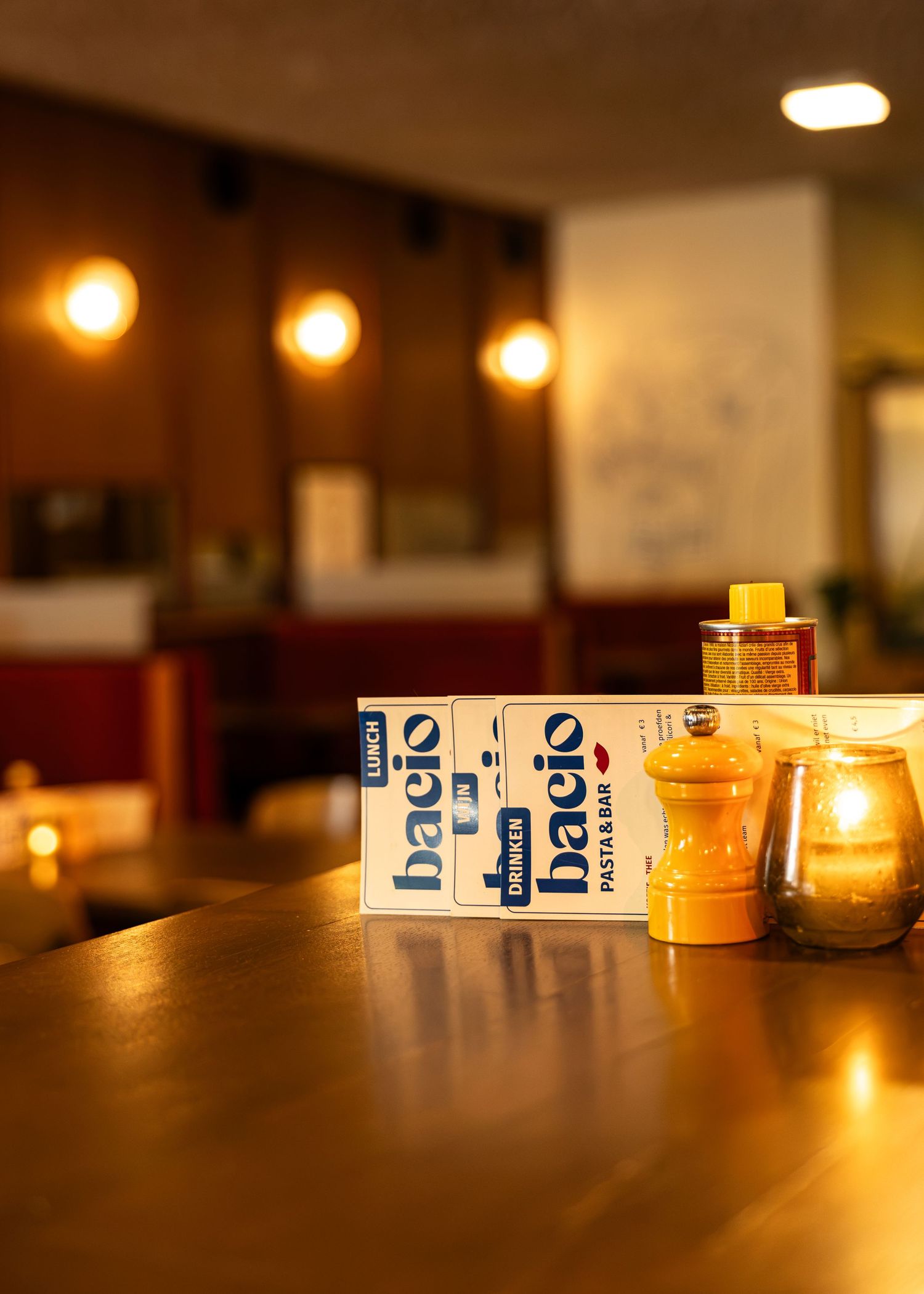 Bacio restaurant menus displayed on a warm wooden table with pepper mill and candle in cozy dining room.