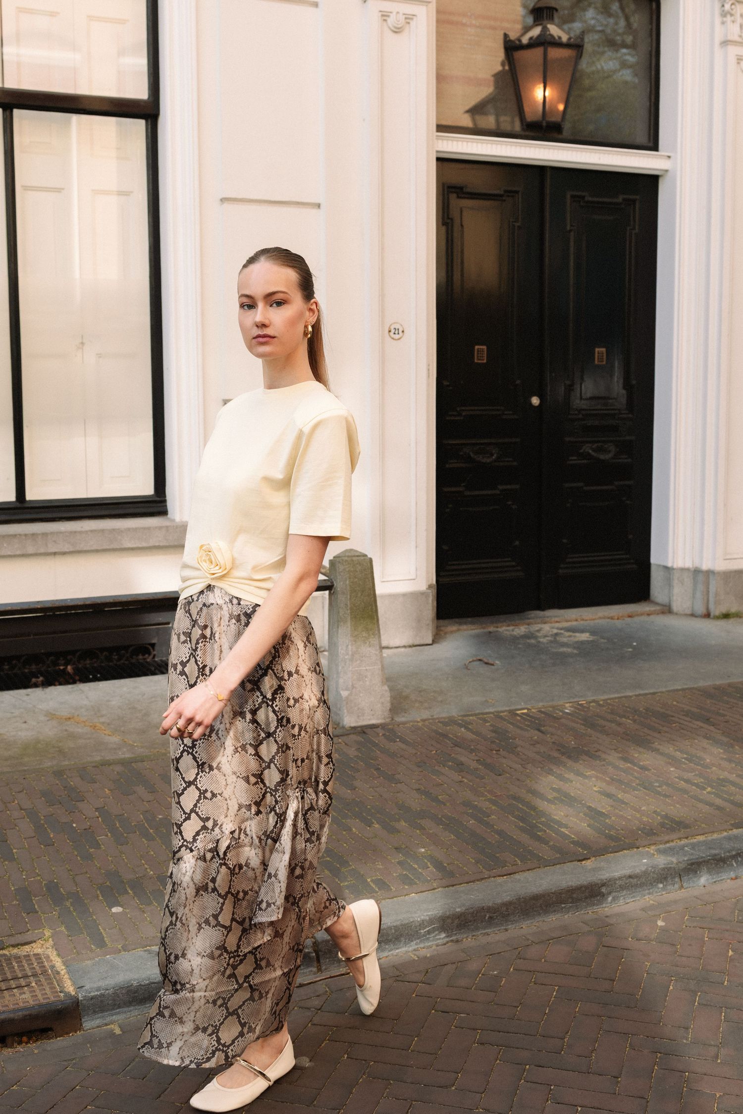 Woman in yellow top and snake print maxi skirt with white flats posing on a cobblestone street.  fashion photography, netherlands