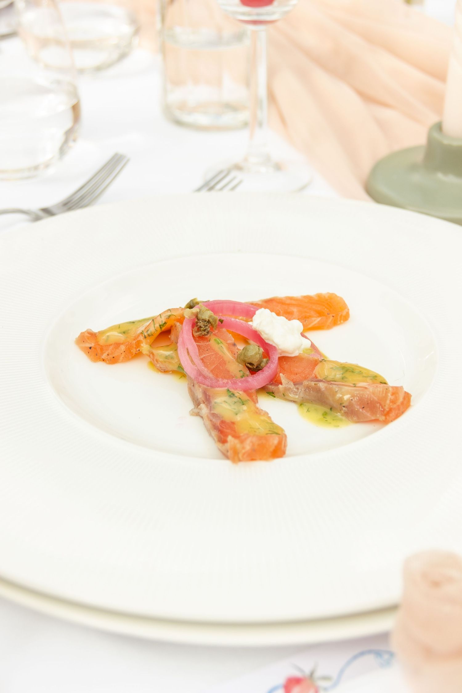 Elegant plated smoked salmon with pickled red onions, capers, and cream cheese on a white dish at a formal dinner. event photography,