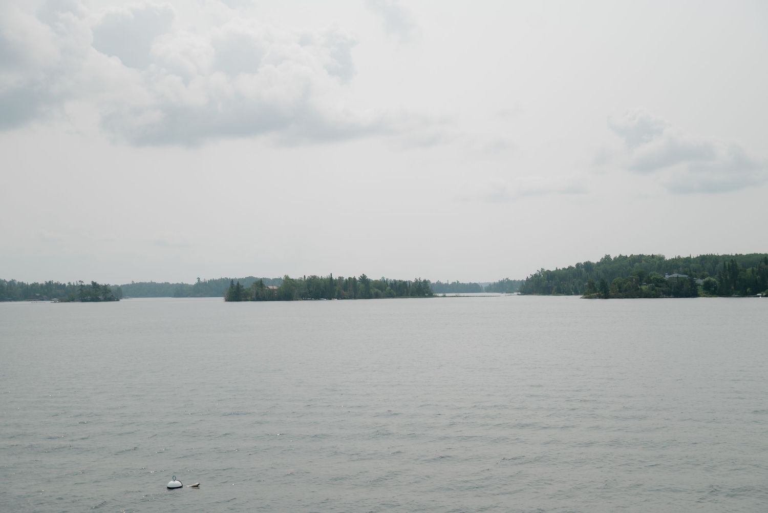 Panoramic view of a calm lake with distant tree-lined shores under cloudy skies.