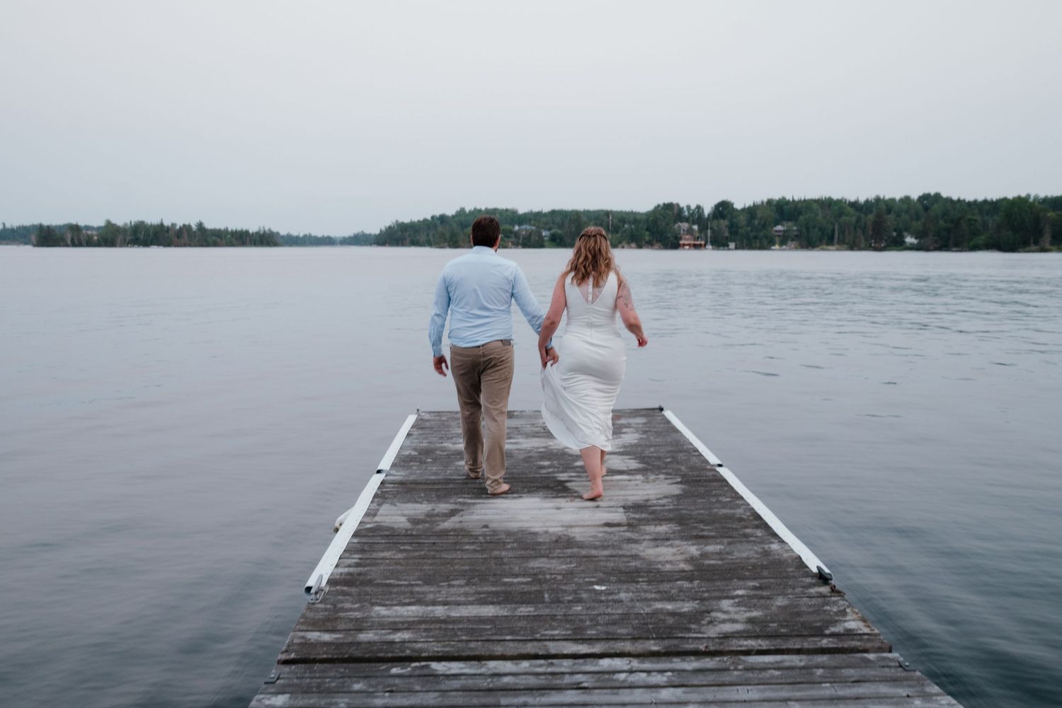 Long wooden dock extending into a serene lake with distant shoreline visible.