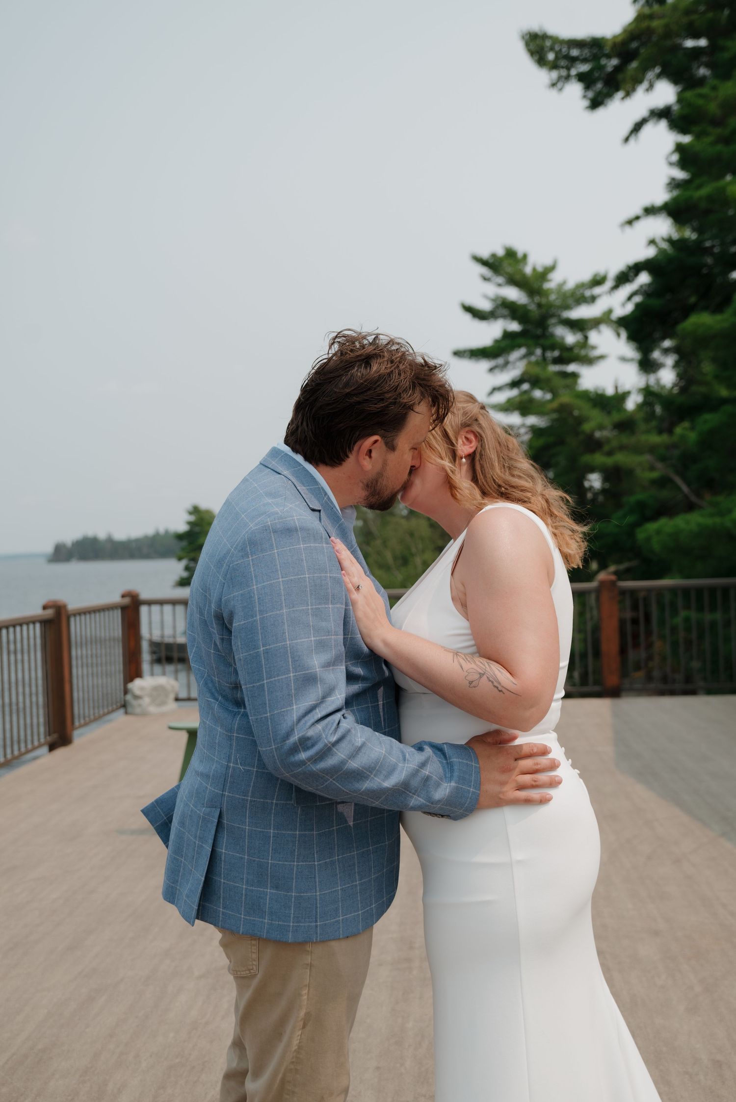 A romantic moment between a couple in formal attire sharing a kiss on a lakeside deck.