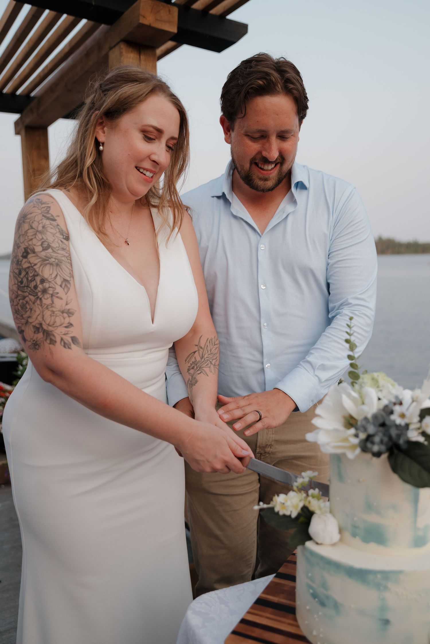 Couple cutting their blue and white wedding cake together at waterfront reception.
