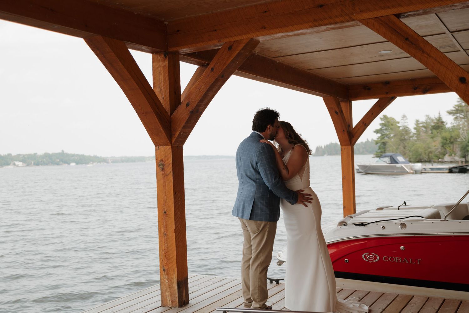 Wedding guests gather under a rustic wooden pavilion by the waterfront during an intimate ceremony.