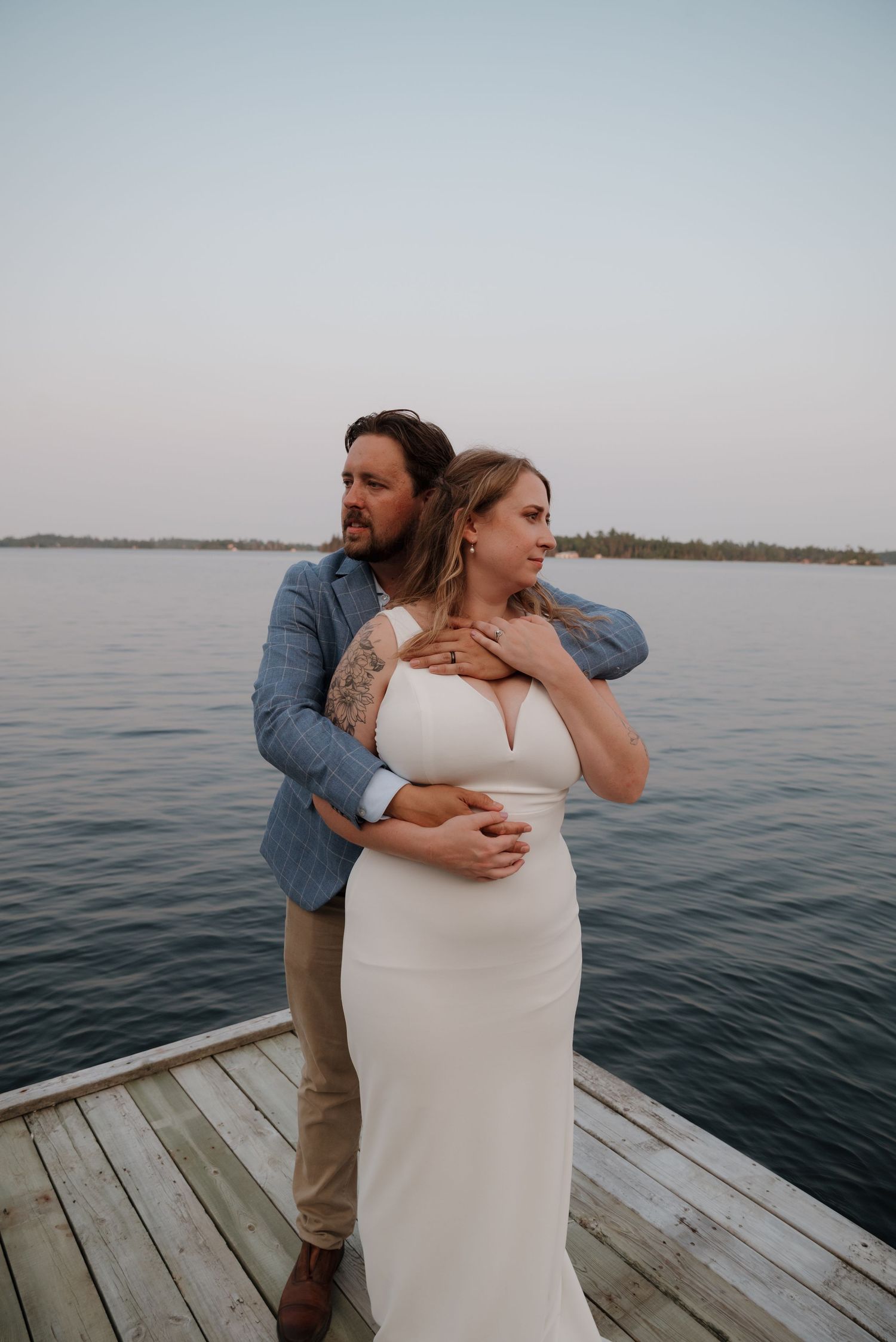 A couple embraces on a wooden dock overlooking a serene lake at dusk.
