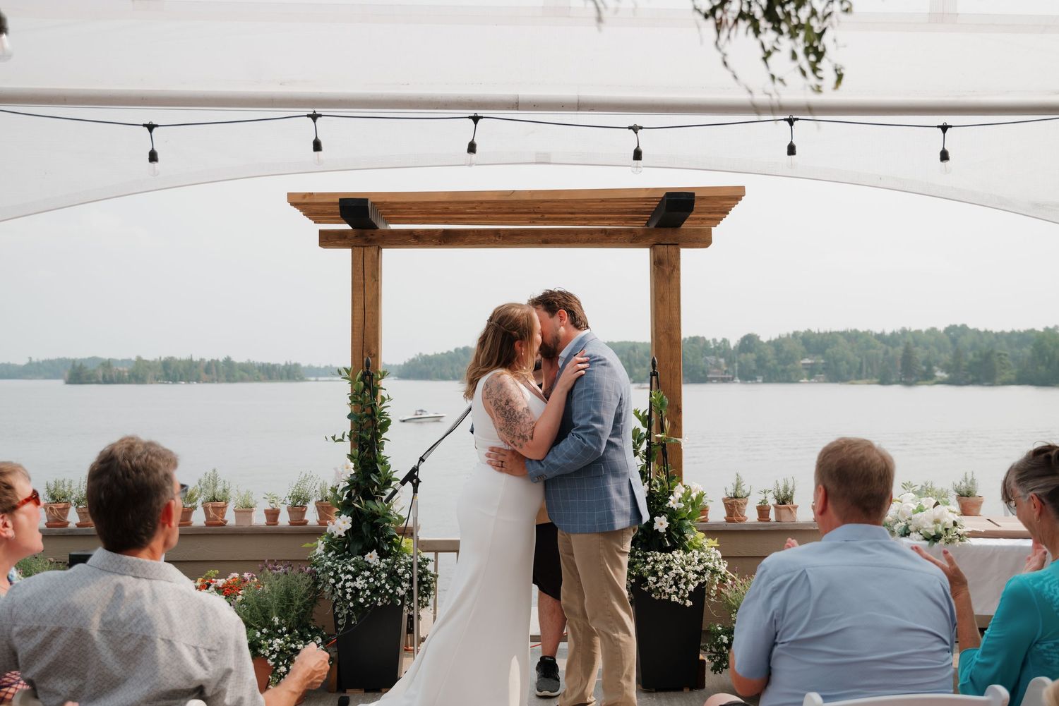 Outdoor wedding ceremony setup with wooden beams and string lights overlooking a serene lake.