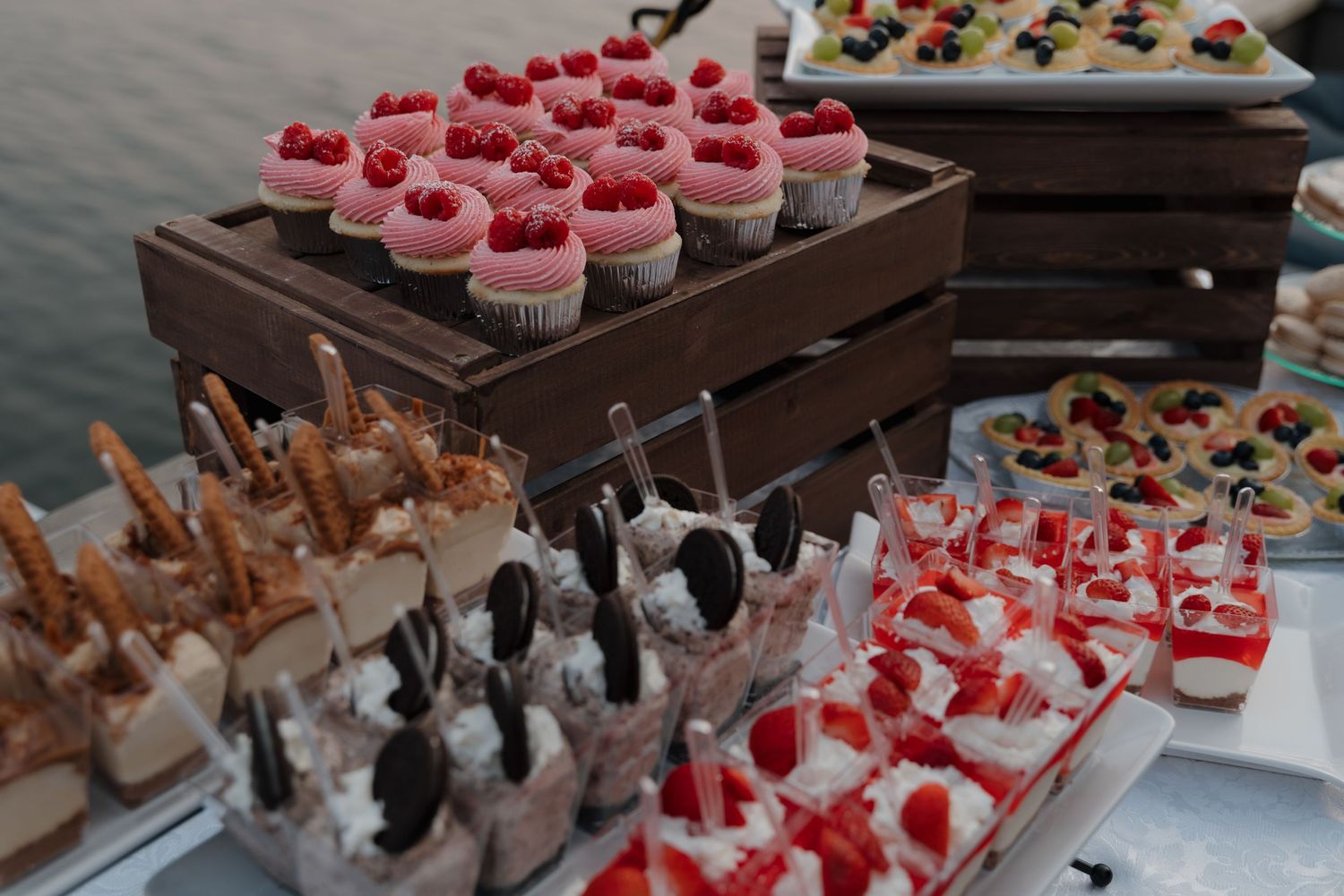 An assortment of pink and white cupcakes and desserts displayed on wooden serving platters at a wedding reception.