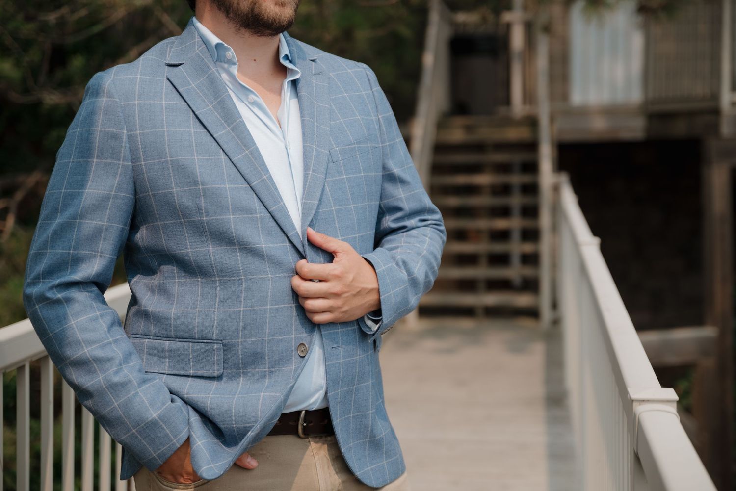 Person in light blue blazer and khaki pants stands on waterfront deck with scenic lake view.