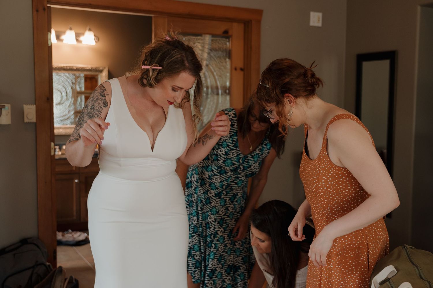 People in formal attire preparing in an indoor room with wooden trim and neutral walls.