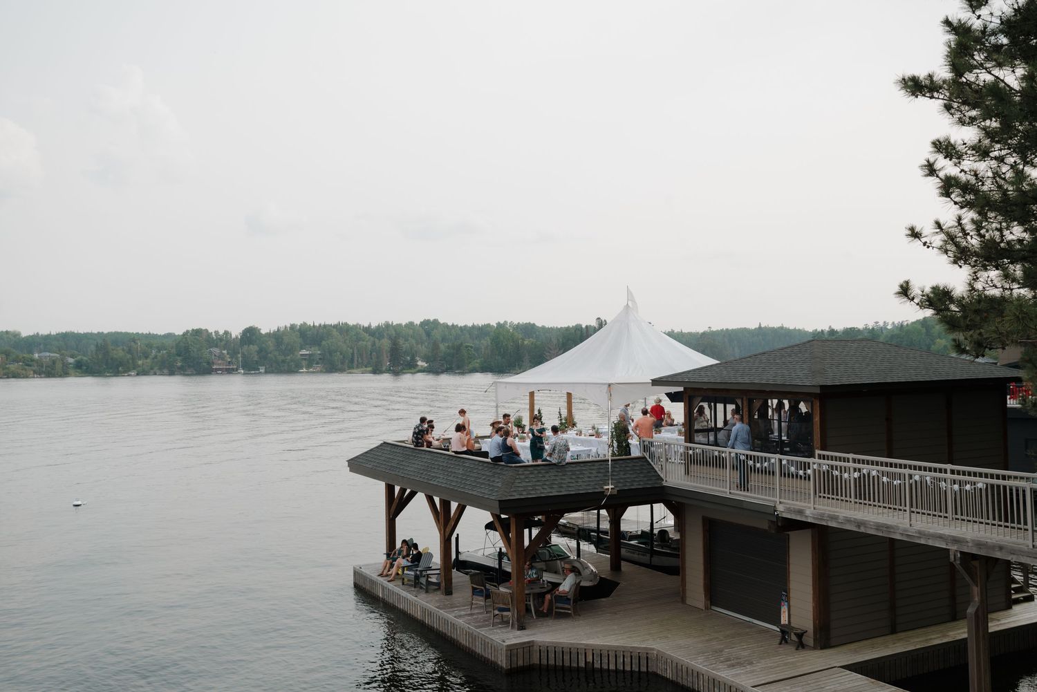 Waterfront wedding venue with white tent and wooden dock extending over calm lake waters.