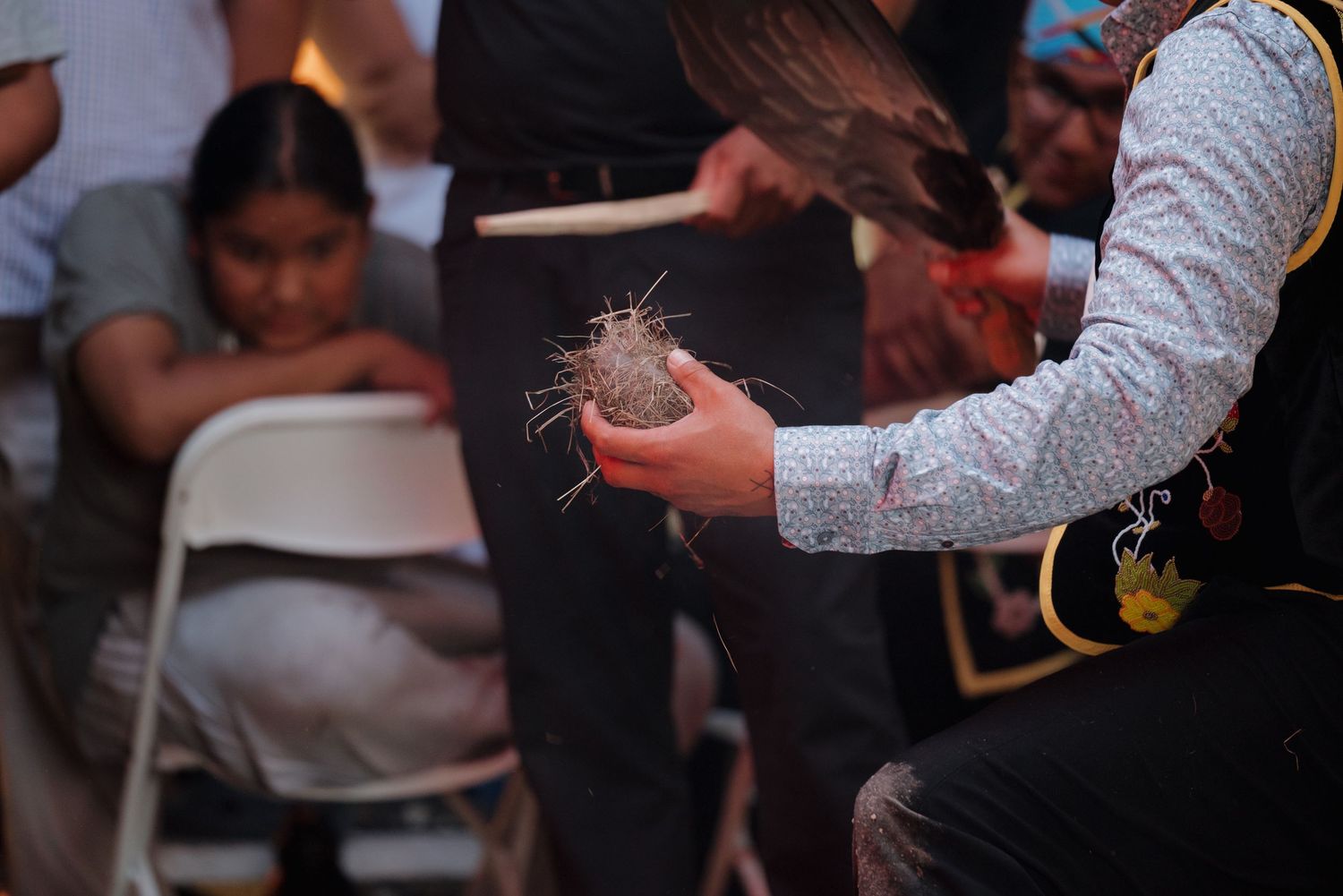 A person holds a woven nest artifact during a cultural gathering event indoors.