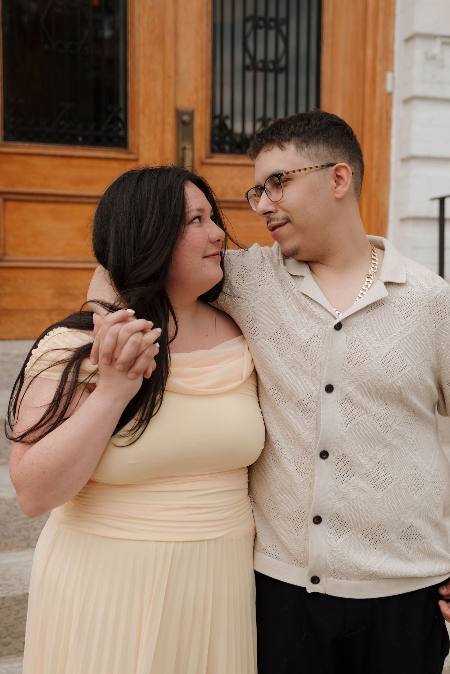 A romantic couple shares an intimate moment in front of an elegant wooden doorway with ornate details.