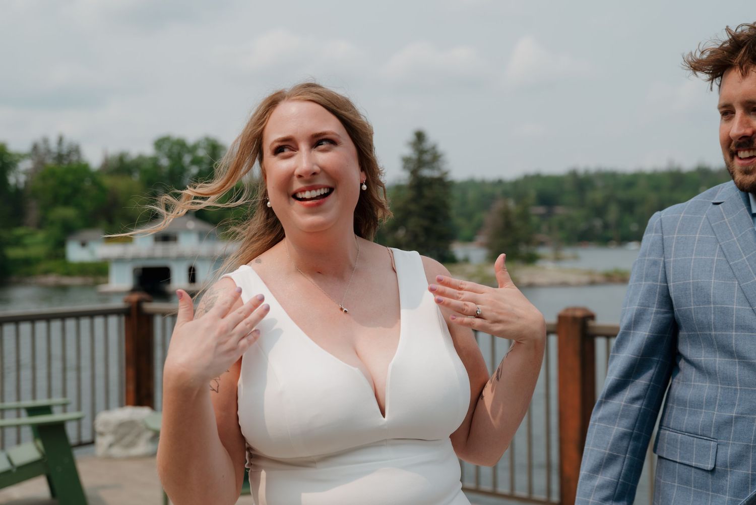 A bride in a white wedding dress twirls on a lakeside deck during a summer celebration.