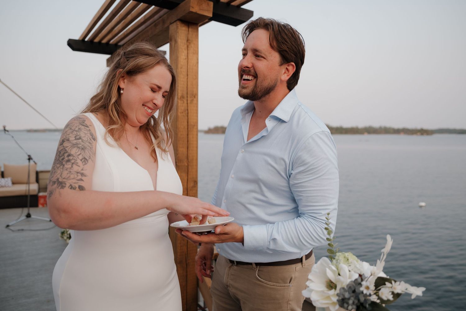 A couple shares an intimate moment during their waterfront wedding ceremony with string lights overhead.
