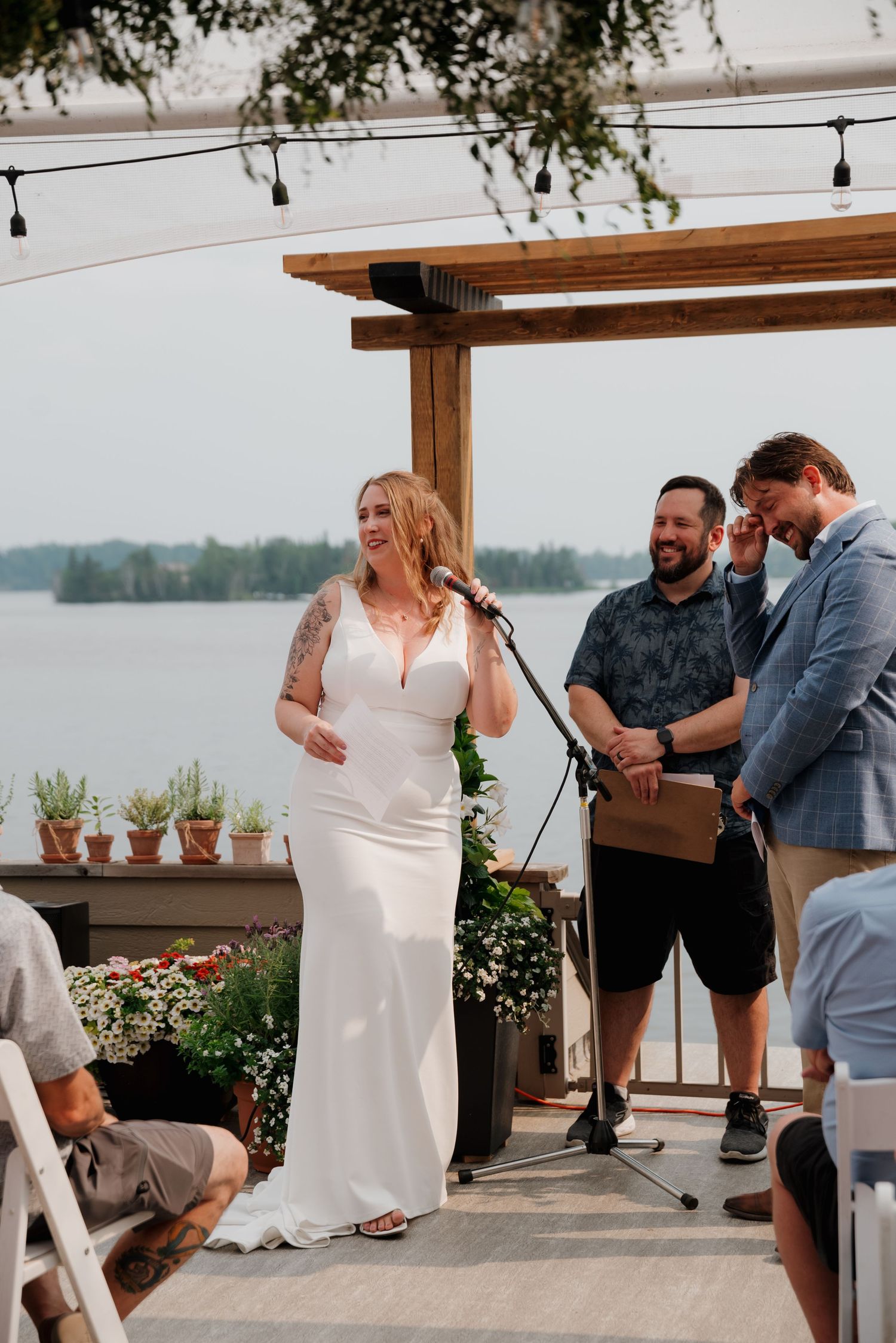 An outdoor wedding reception setup with string lights and lakefront views.
