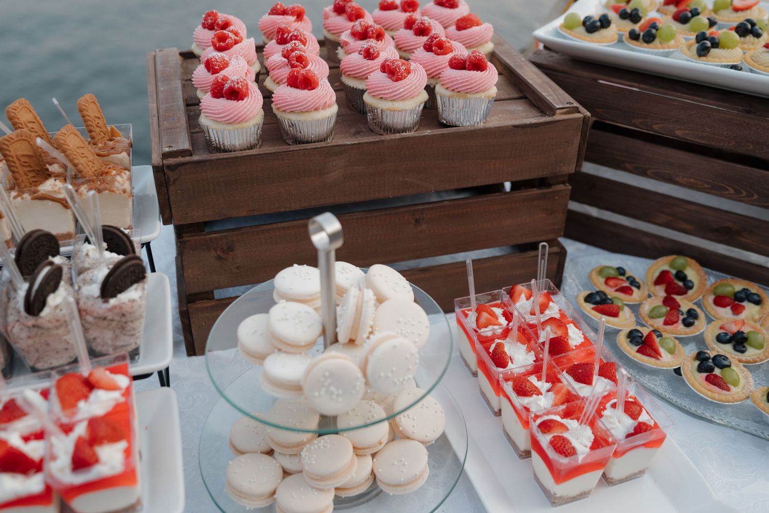 An assortment of pink frosted cupcakes and pastries arranged on tiered wooden display stands.