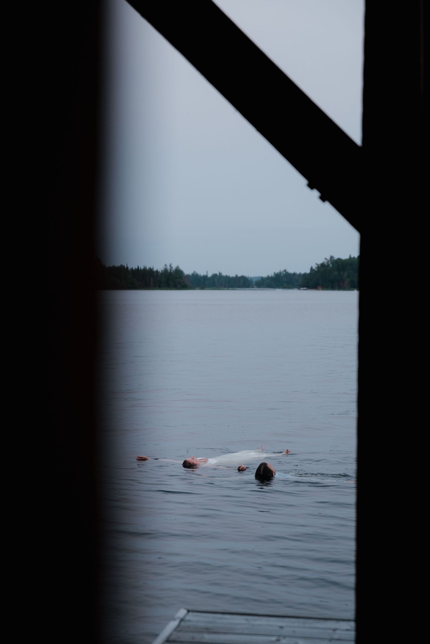 A swimmer floating in a calm lake surrounded by distant trees and shoreline.