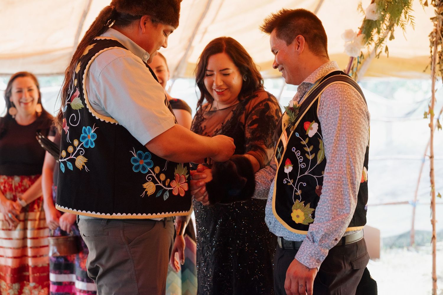 Three people in traditional embroidered vests sharing a joyful moment during a cultural ceremony.