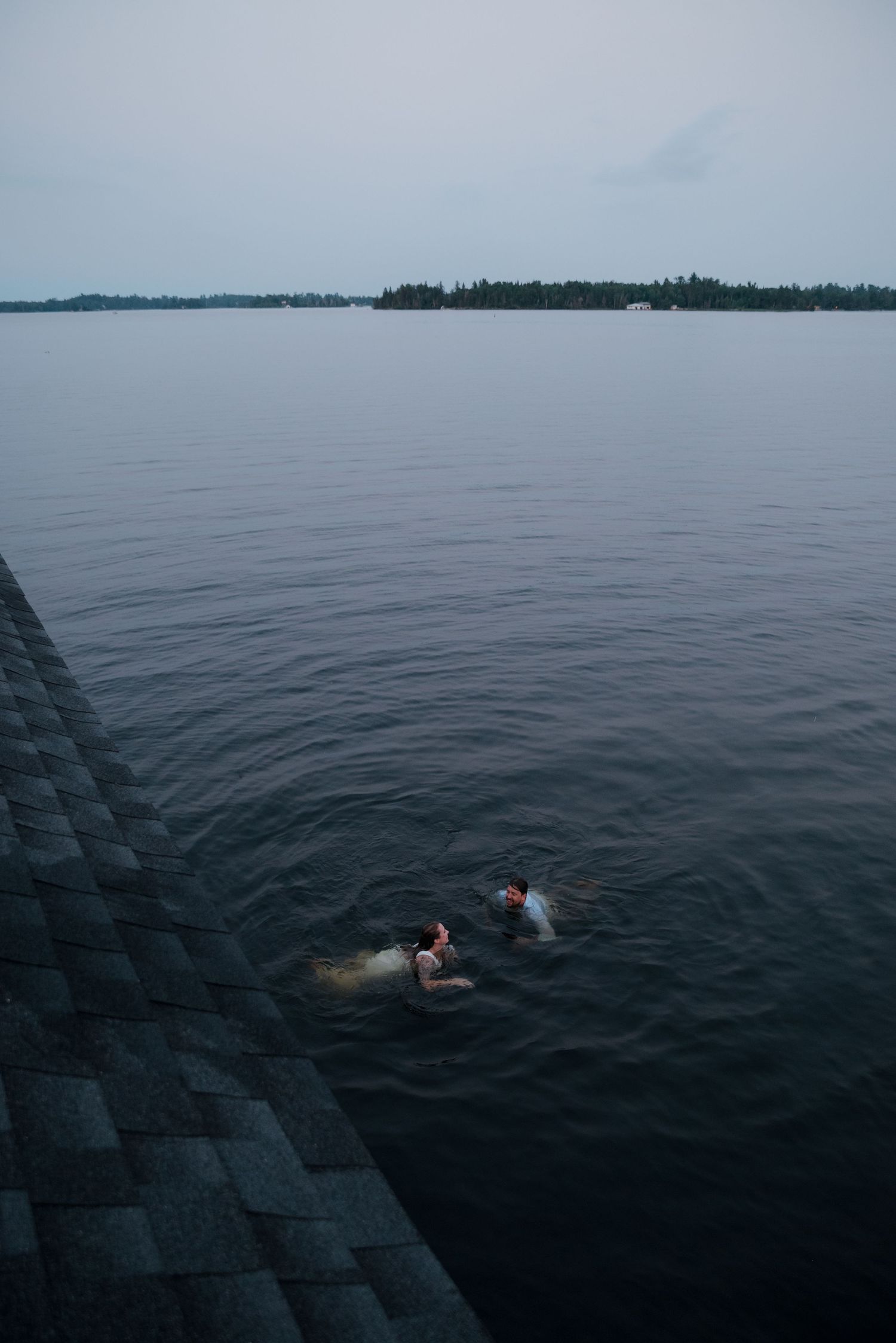 People swimming in a dark lake with distant shoreline visible on the horizon.